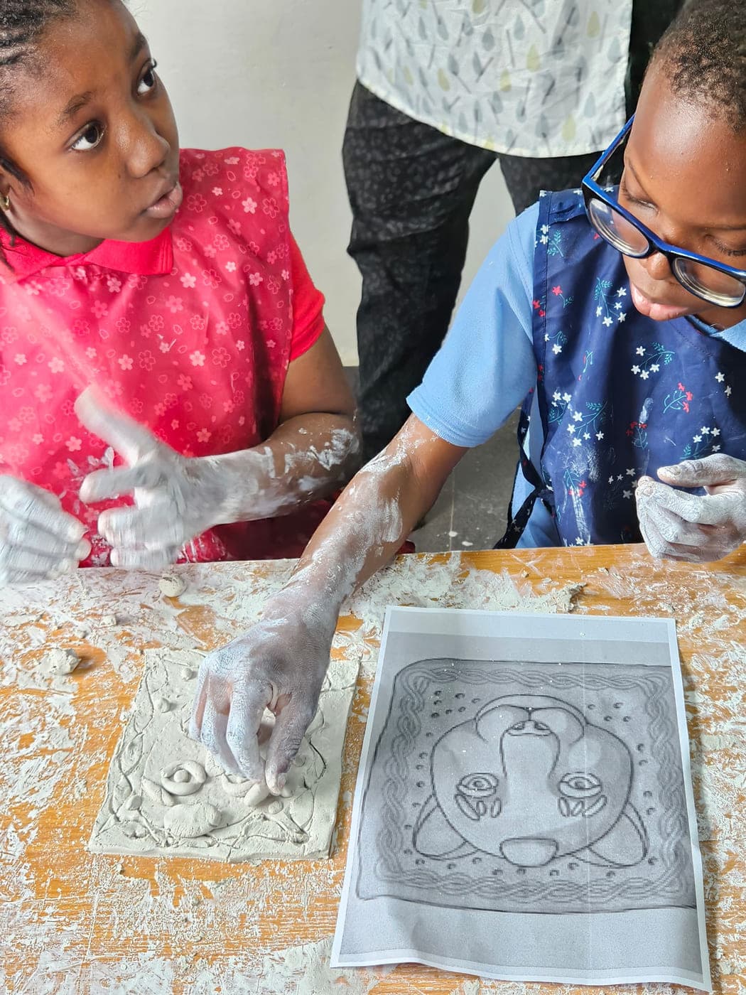 Pupils pressing a design into a clay tile at the craft table