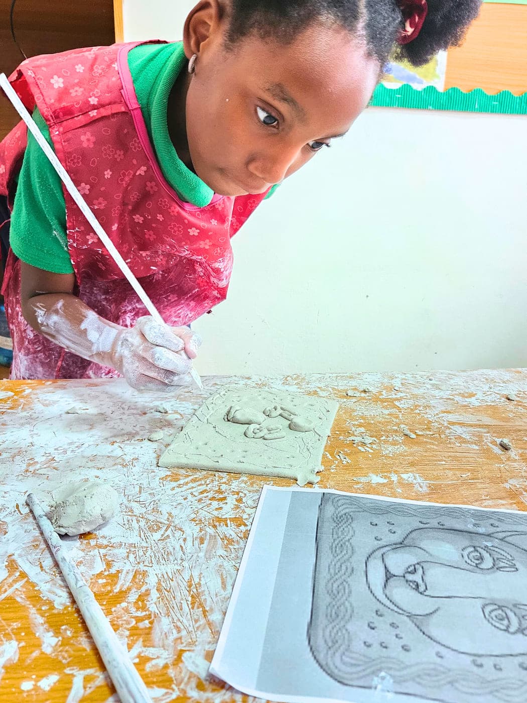 A pupil smoothing the surface of the clay relief she has carved