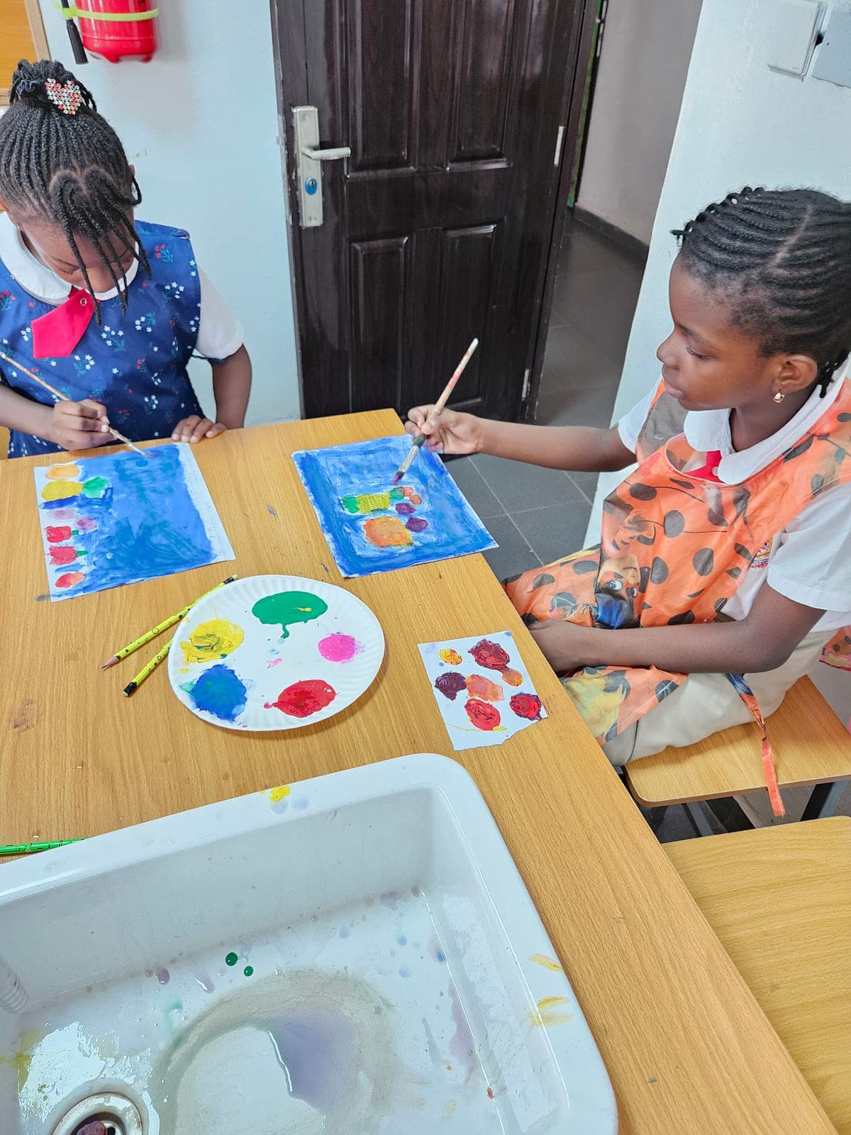 Two pupils working side by side over their paint palettes in the art room