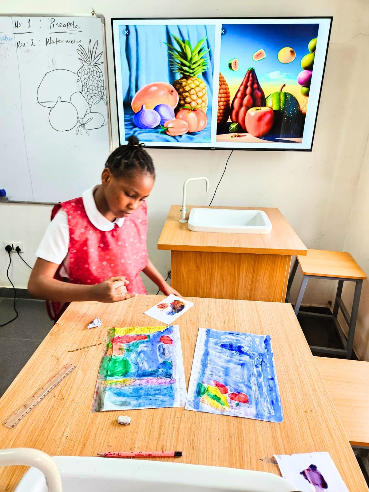 A pupil painting a still life from the fruit study displayed on the classroom screen