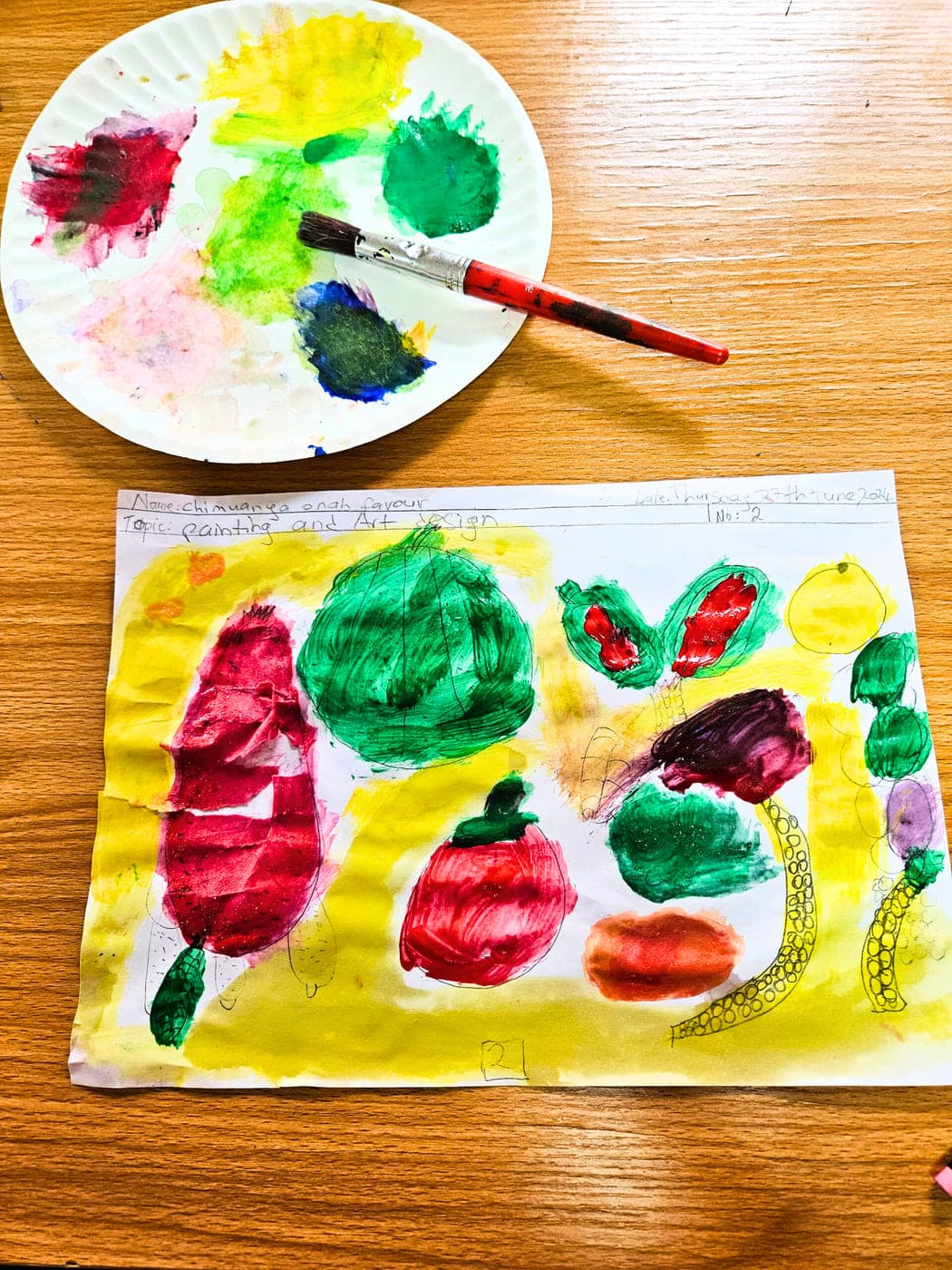 A finished vegetable painting laid out beside the palette and brush that made it