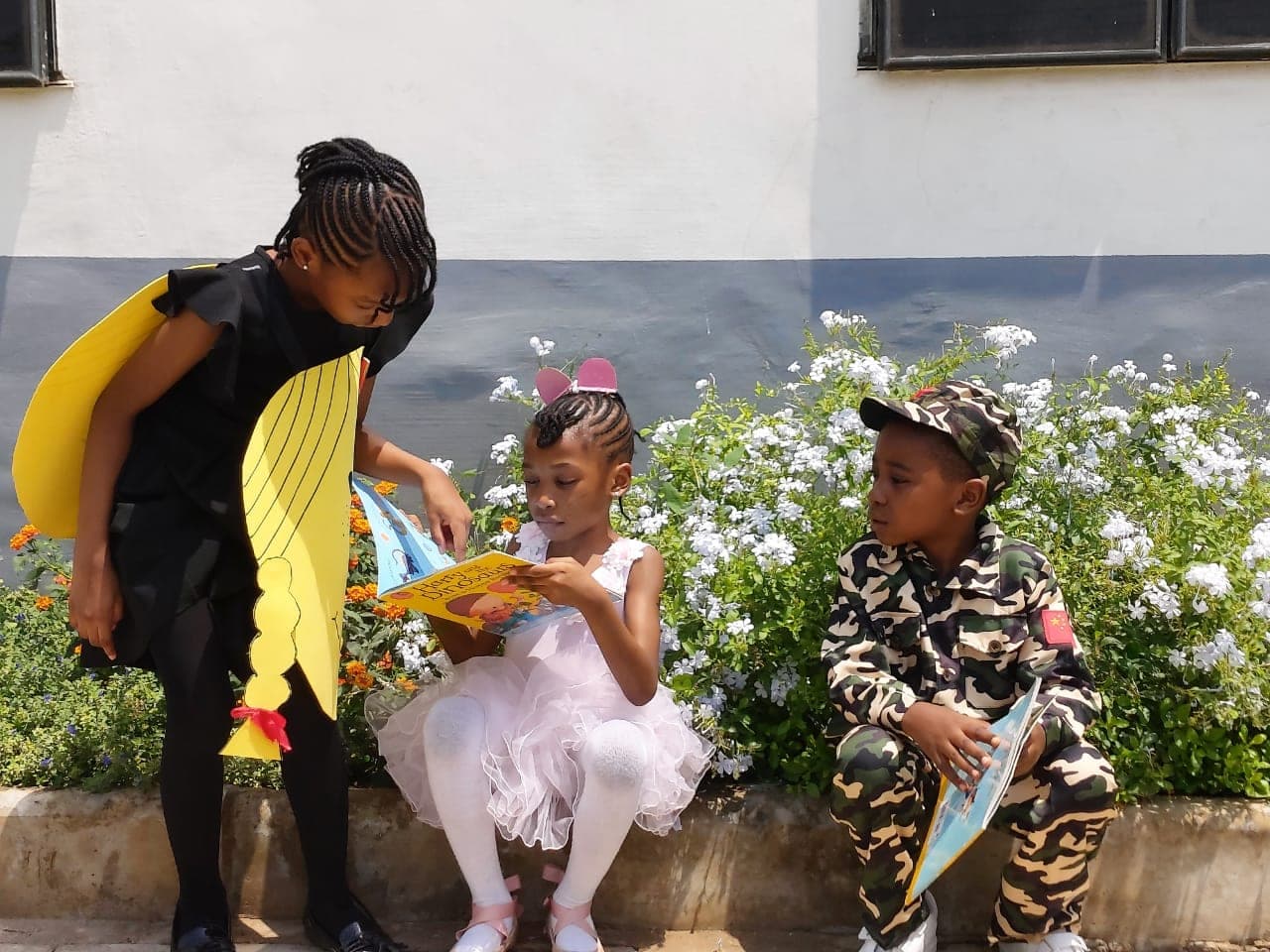 Children in storybook costumes reading together on the garden wall