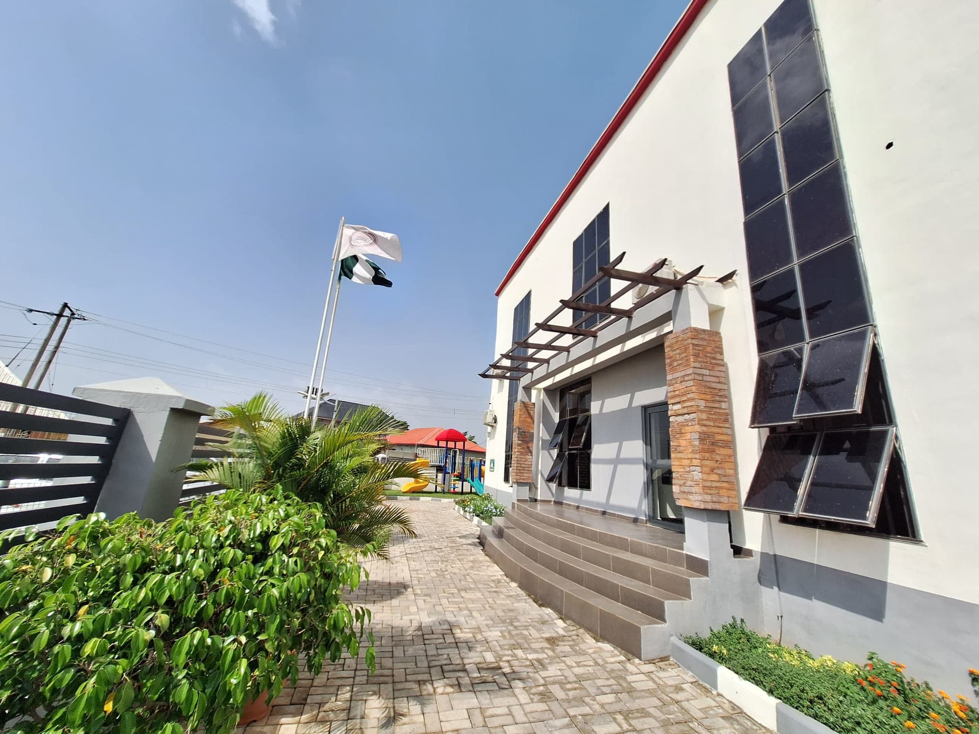 Solar panels ranged along the school roofline above the paved courtyard, with the national flag flying