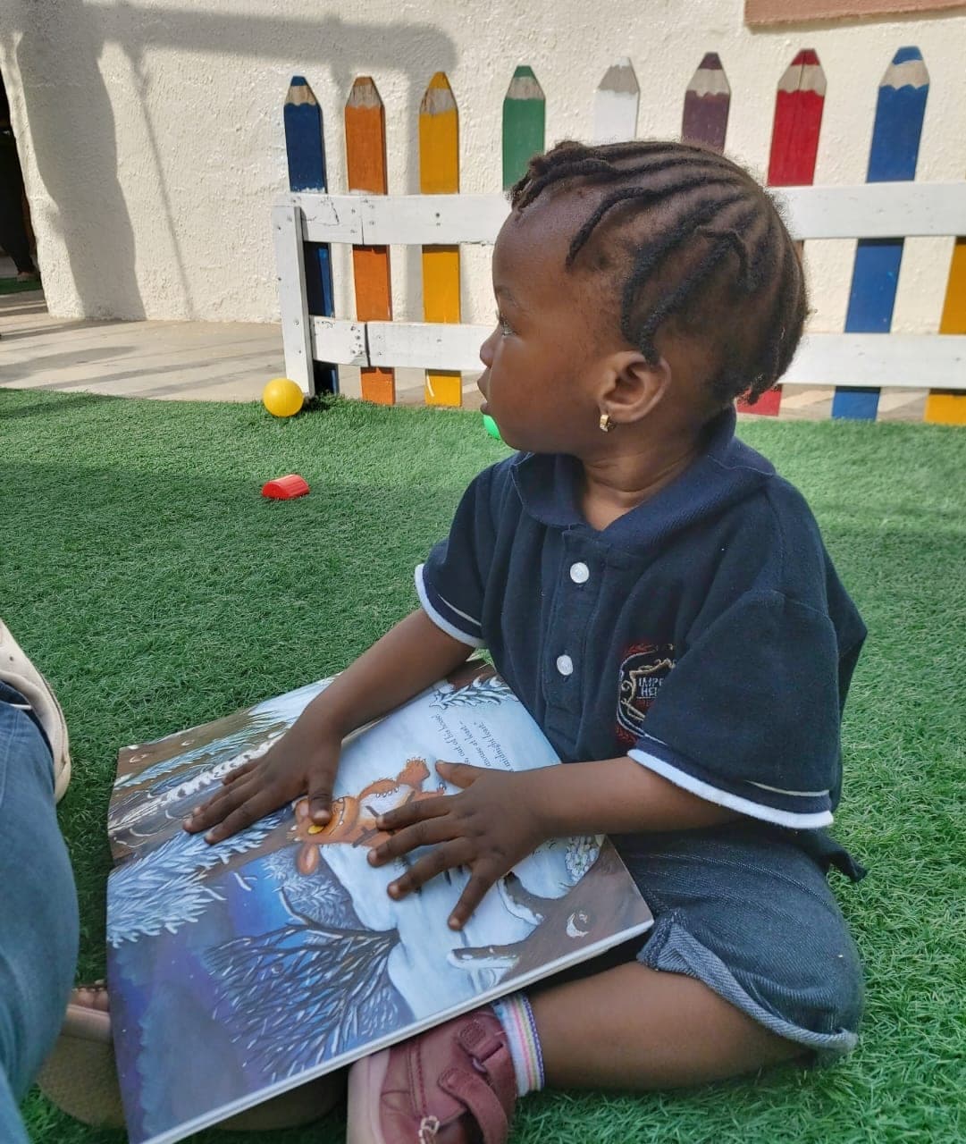 A toddler turning the pages of a picture book on the playground turf