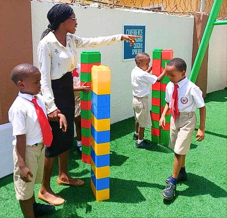 A teacher and two pupils building a tower from giant coloured blocks outdoors
