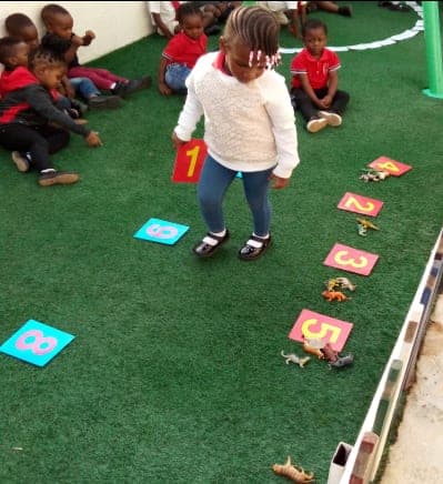 A child hopping between number cards laid out on the playground turf