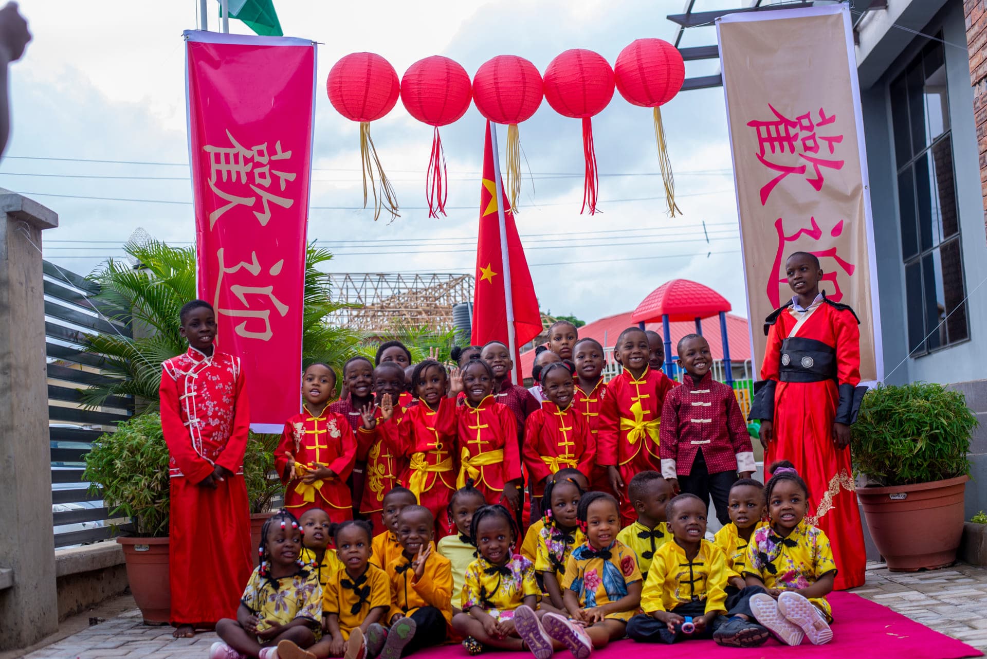 The full Cultural Day cast in red and gold costume beneath the lanterns