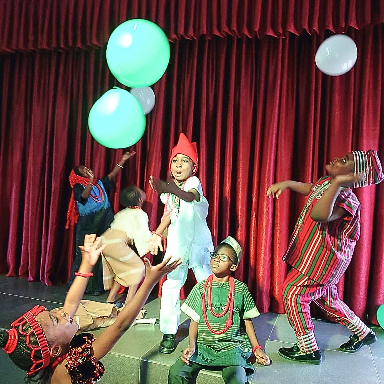 A lively scene from a school play, balloons rising above the stage
