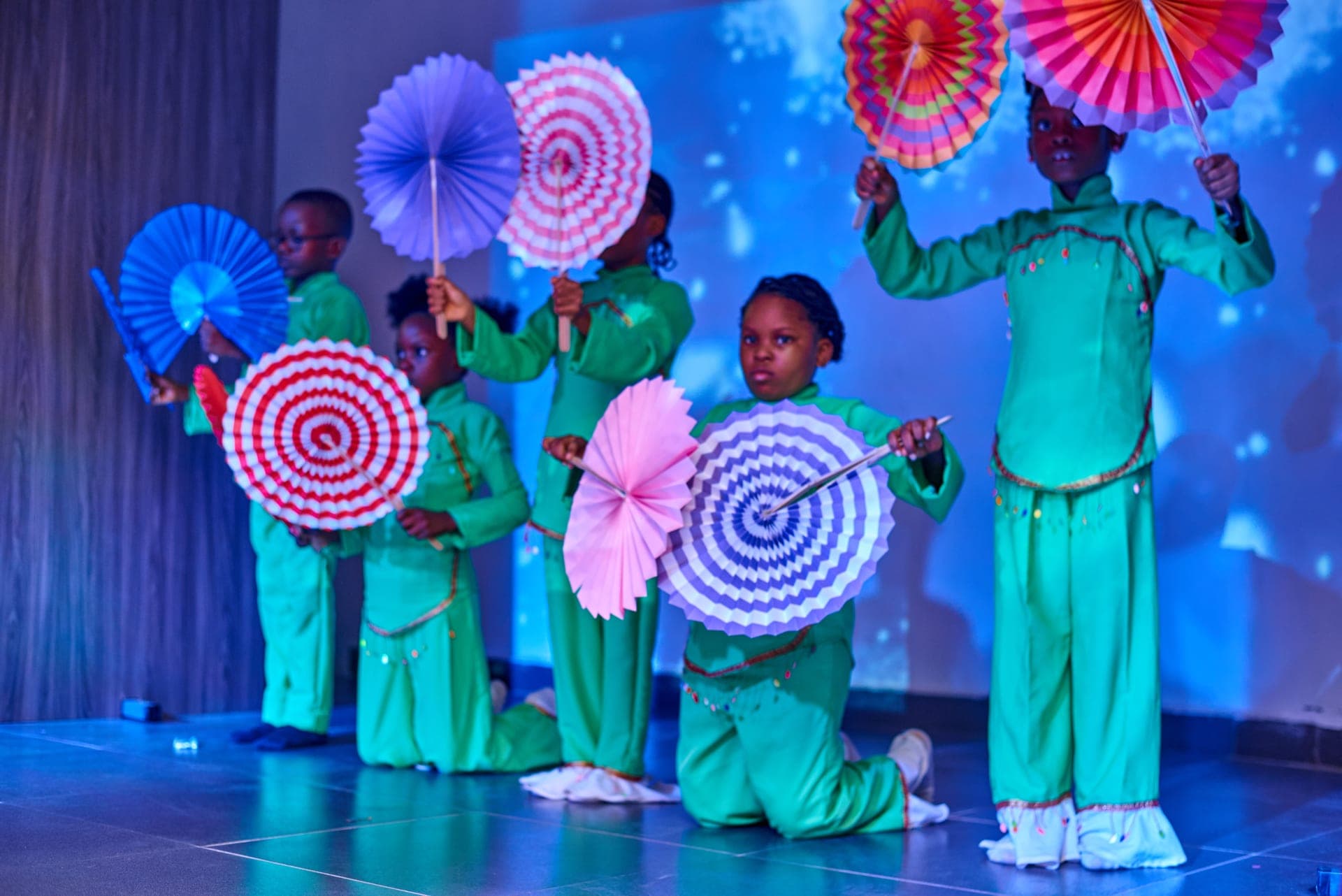 Pupils performing a fan dance under stage lights in our cultural production