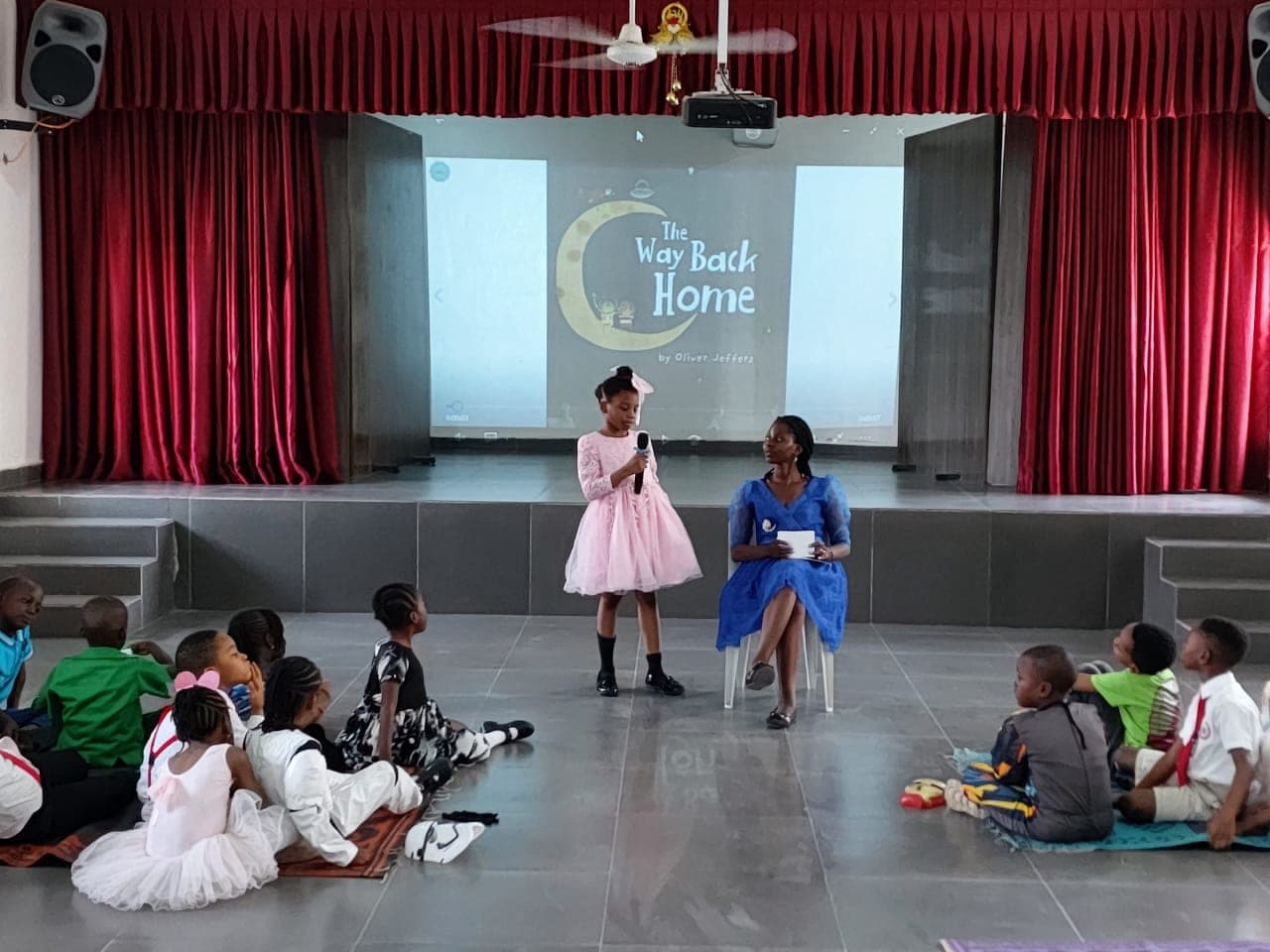 A pupil performing in the school hall while classmates watch from the floor