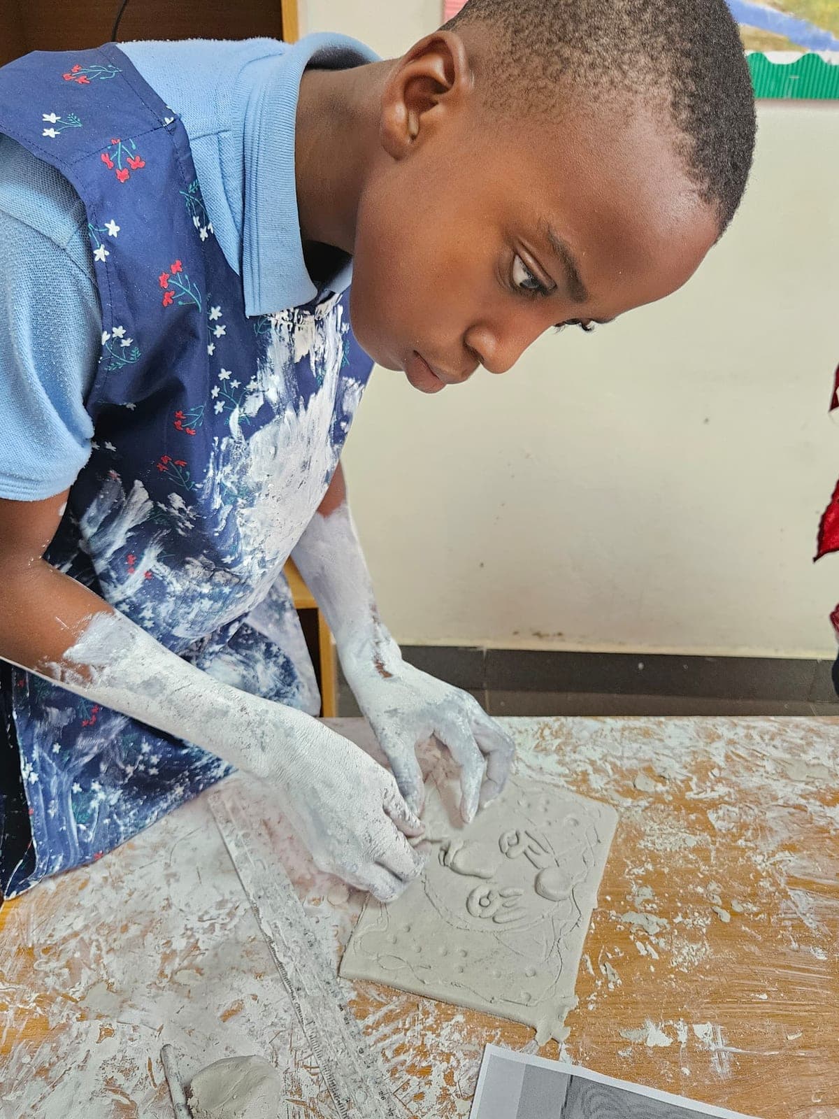 A boy pressing a pattern into a clay tile in the art room