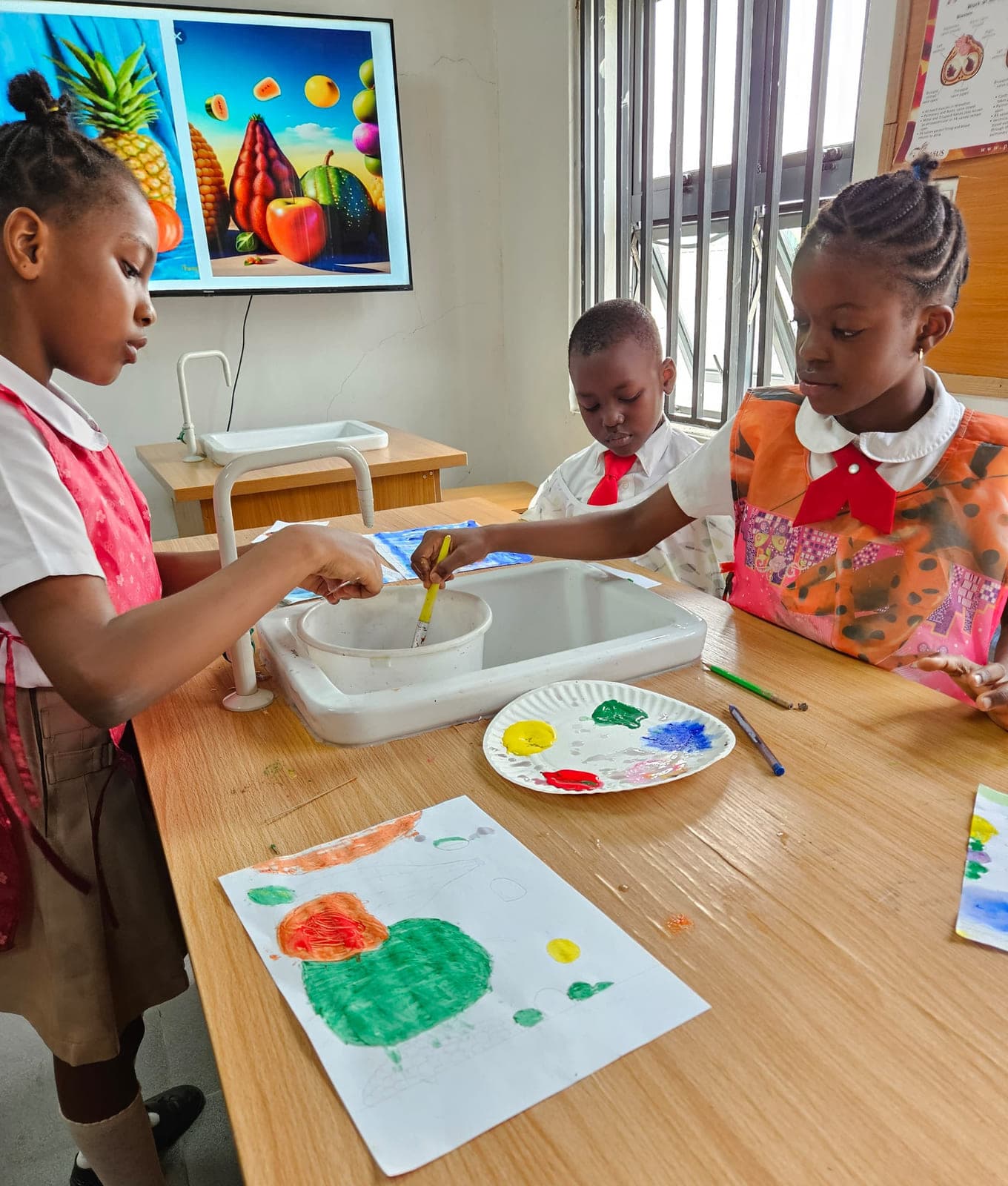 Pupils mixing colour at the art table while they paint the fruit study on the classroom screen