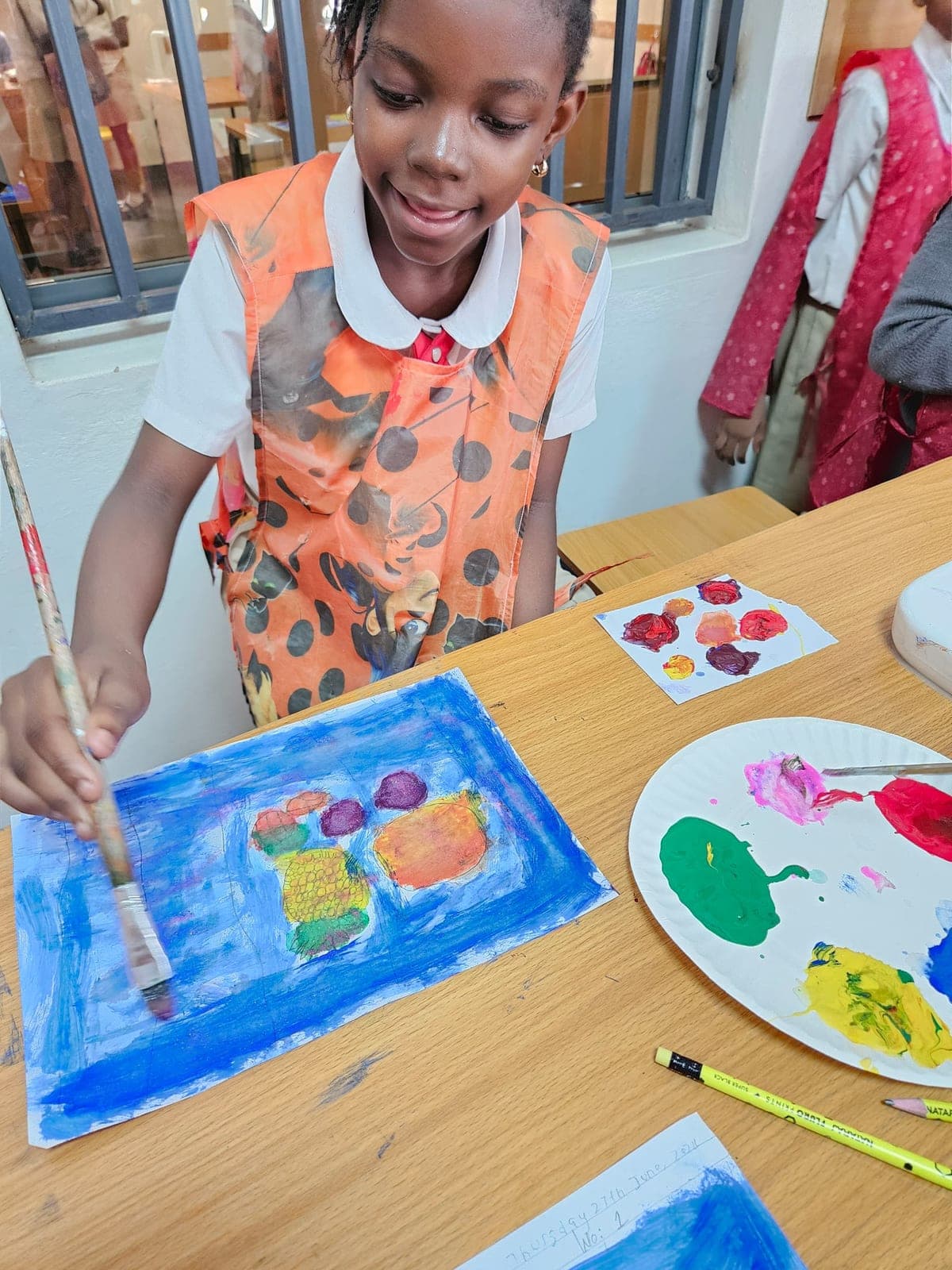A boy in an art apron painting at the table with his palette beside him