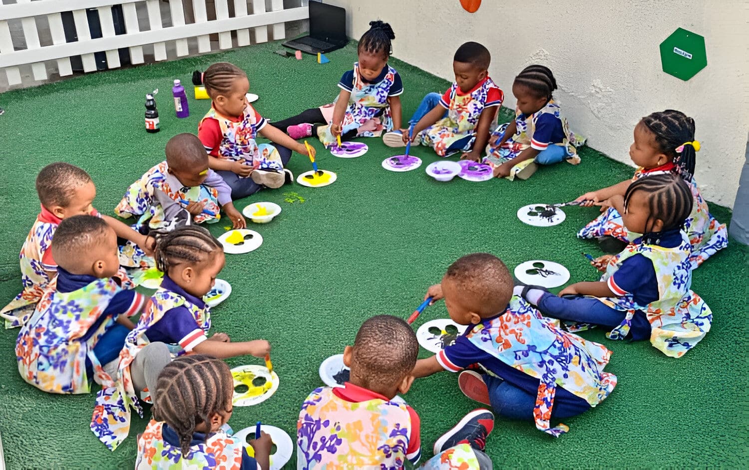 Our youngest children in art smocks, seated in a wide circle to paint on the turf