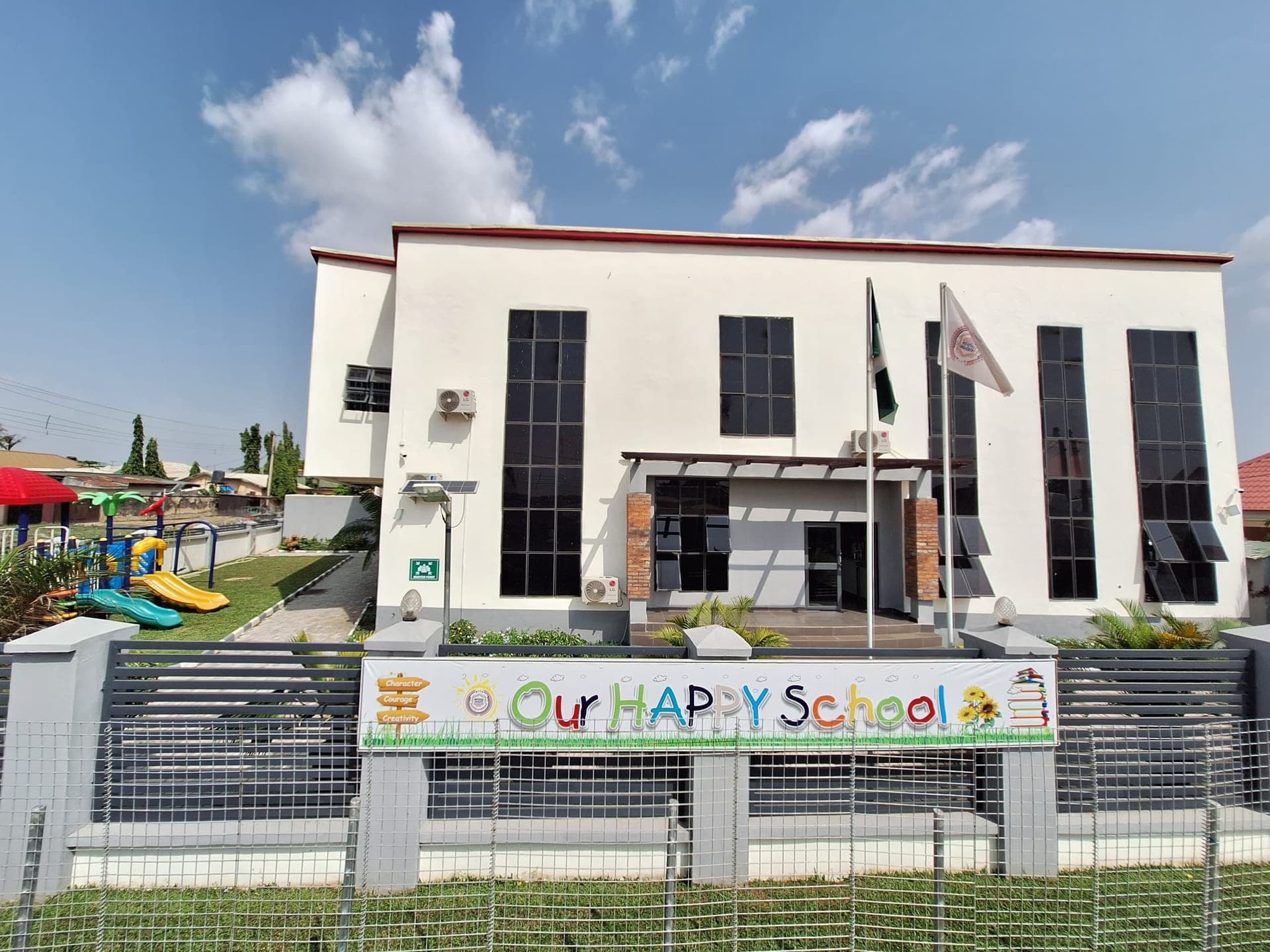 The front of the Imperial Heights campus, with the 'Our Happy School' sign and playground behind the railings