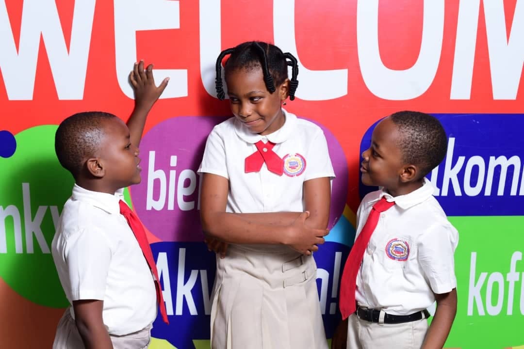 Three pupils in front of a backdrop reading 'welcome' in many languages