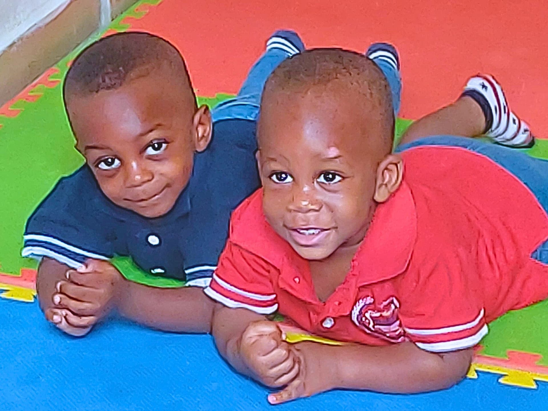 Two crèche toddlers lying side by side on the soft play mat