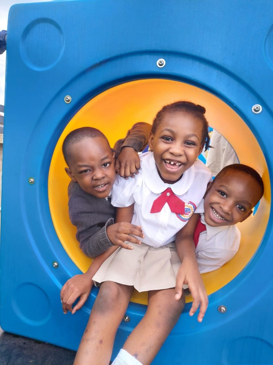 Three delighted children peering out of the playground tunnel window