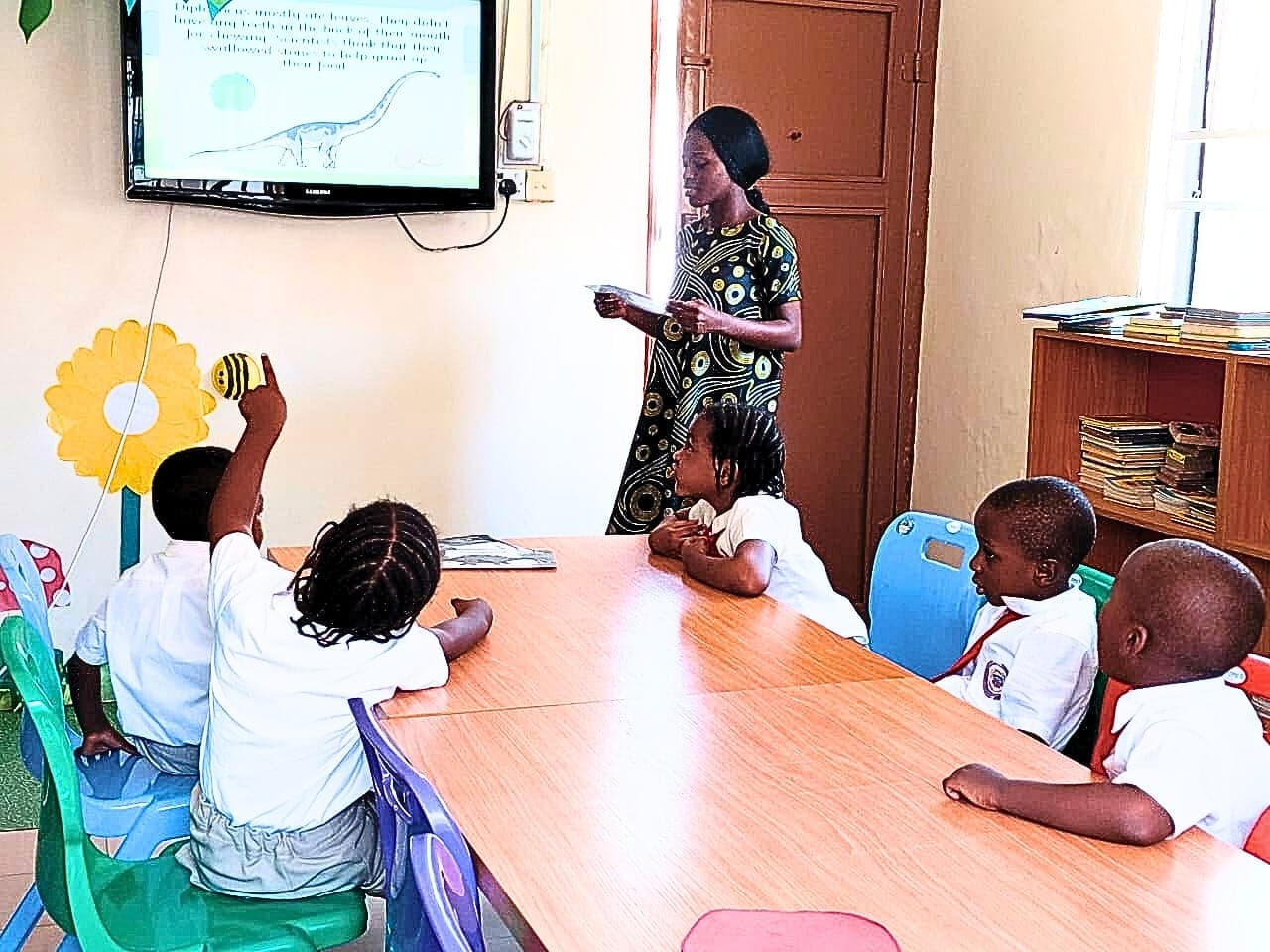 An Early Years teacher leading a lesson at the interactive screen while children answer from the table